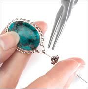 Flat-nose pliers. A hand holding a cabochon, set in a cinch mount that is threaded through an eyepin and a large silver rondelle bead by beading wire. 